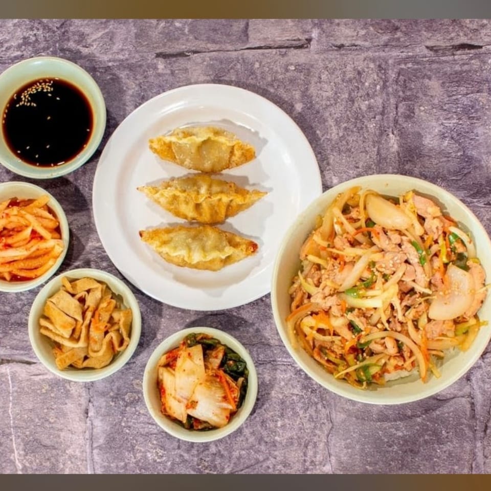J's Korean Food spread with dumplings, kimchi, side dishes, and a large bowl of stir-fried meat and vegetables.