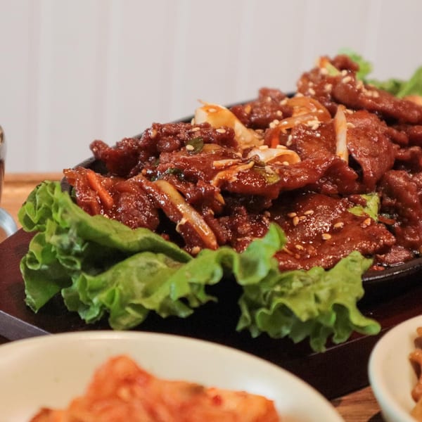 J's Korean Food's spicy pork bulgogi, garnished with sesame seeds and green onions, on a bed of lettuce.